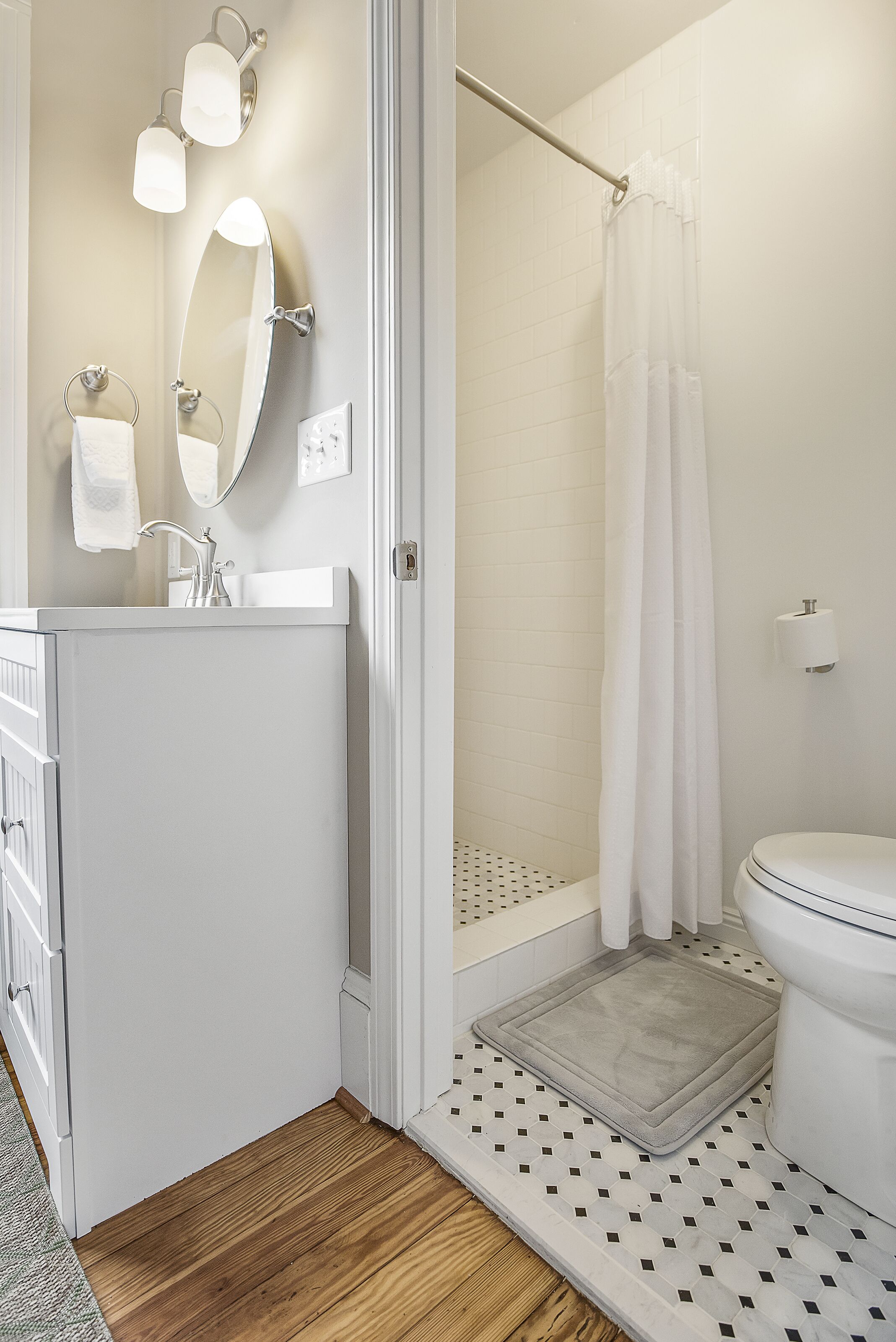 A bathroom with a white sink, mirror, and toilet, a shower with a curtain, and a patterned floor.
