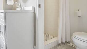 A bathroom with a white sink, mirror, and toilet, a shower with a curtain, and a patterned floor.