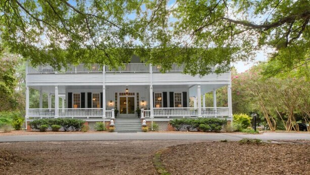 A white, two-story house with a front porch, surrounded by trees and shrubs. - Liberty Hall Bed and Breakfast (Pendleton)