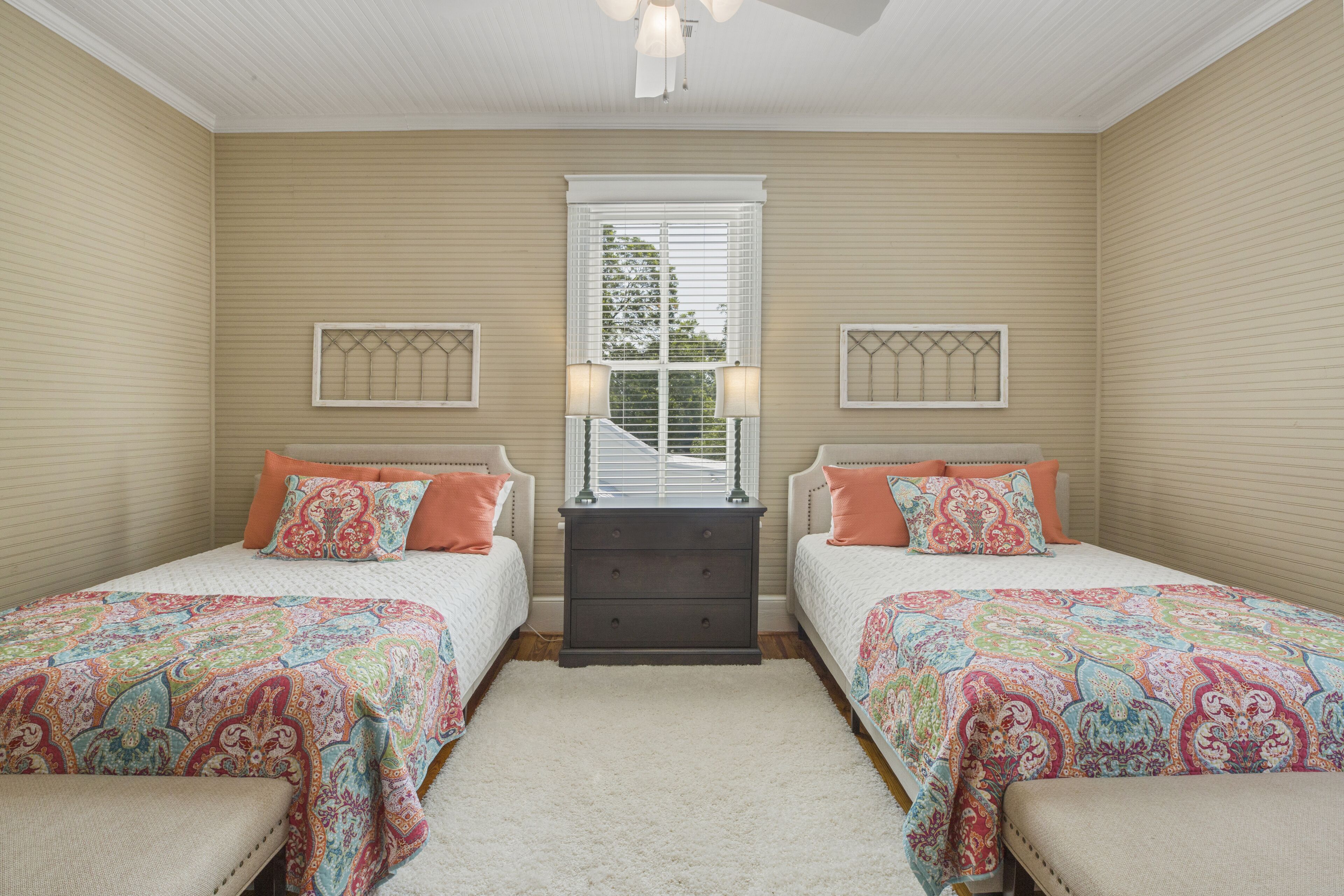 A bedroom with two beds, a dresser, and a window with blinds.