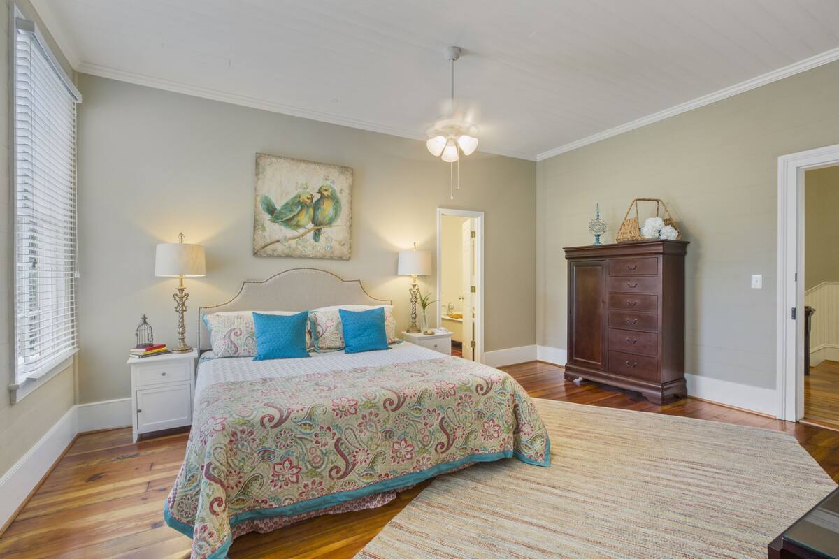 A bedroom with a bed, nightstands, a dresser, a painting, and a chandelier.
