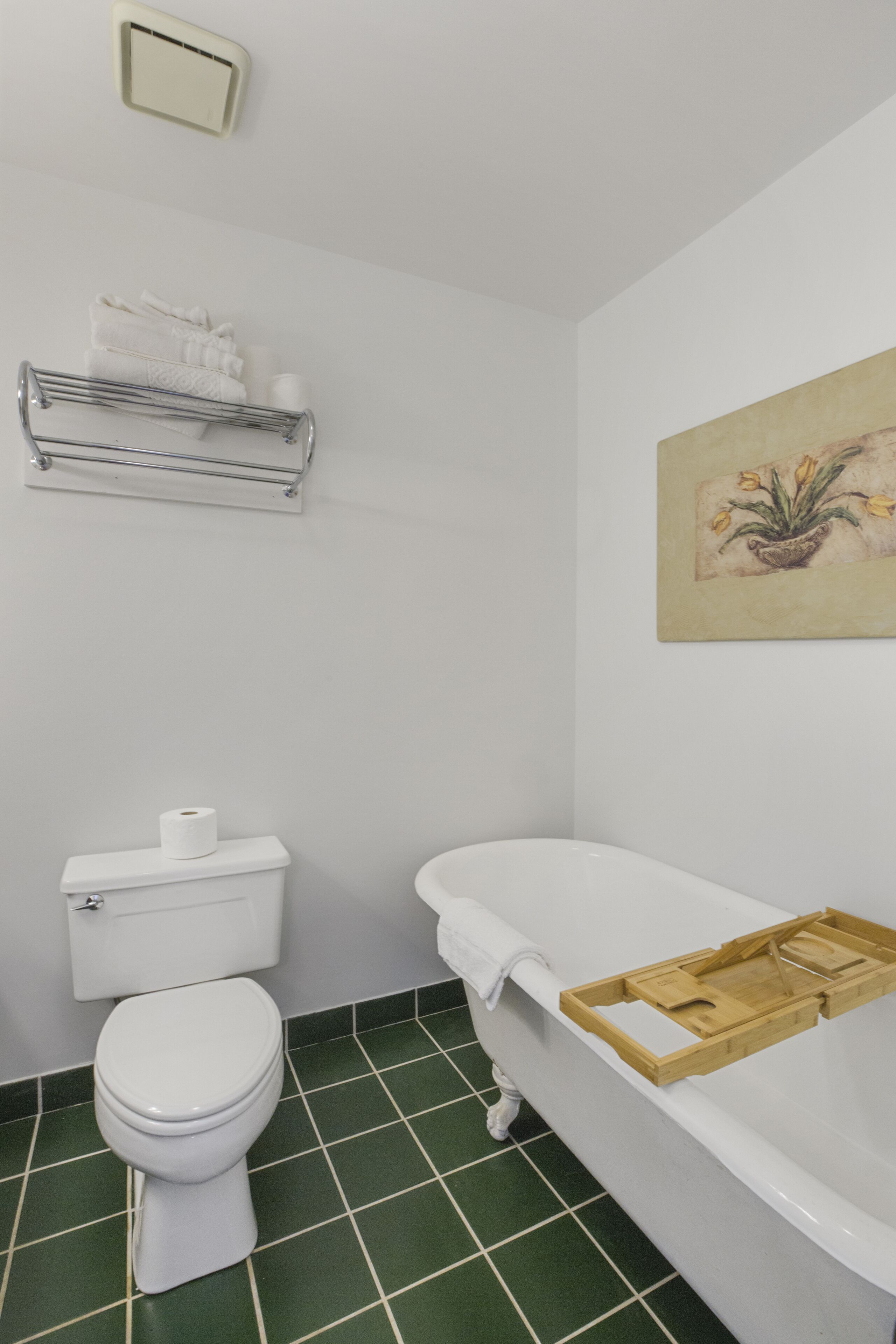 A bathroom with a toilet, a bathtub, a towel rack, and a painting on the wall.
