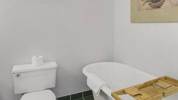 A bathroom with a toilet, a bathtub, a towel rack, and a painting on the wall.