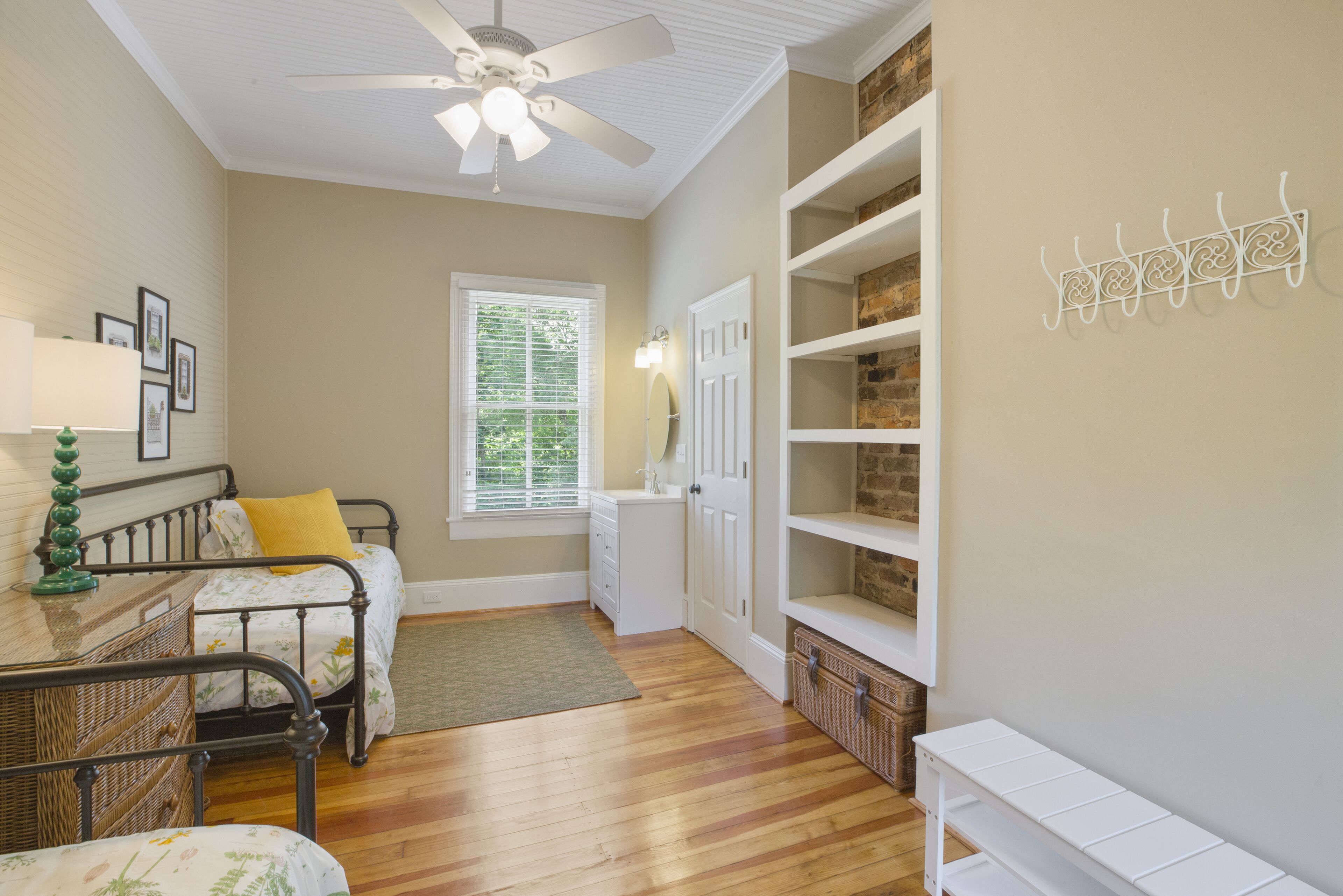 A bedroom with a bed, a dresser, a vanity, a ceiling fan, and built-in shelving.