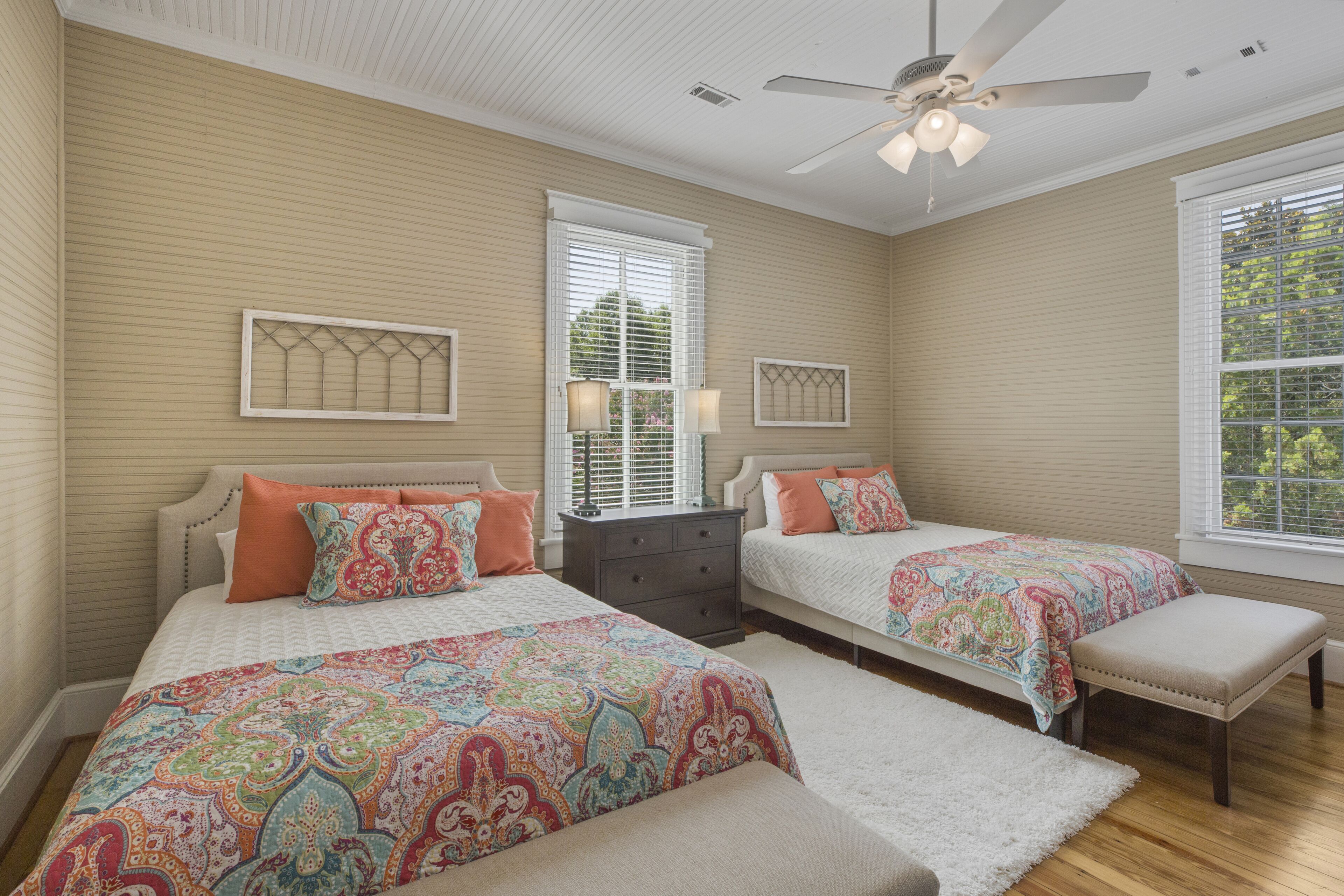 A bedroom with two beds, a ceiling fan, and large windows.