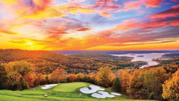 Un campo de golf con vistas panorámicas a un lago y colinas boscosas durante el atardecer.