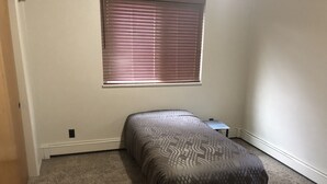 A small, carpeted room with a single bed, a window with blinds, and a small table. - Last minute opening for Cheyenne Frontier Days! (Cheyenne)