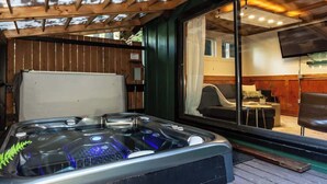 Un jacuzzi con techo de madera y vista a una sala de estar a través de una puerta de vidrio.