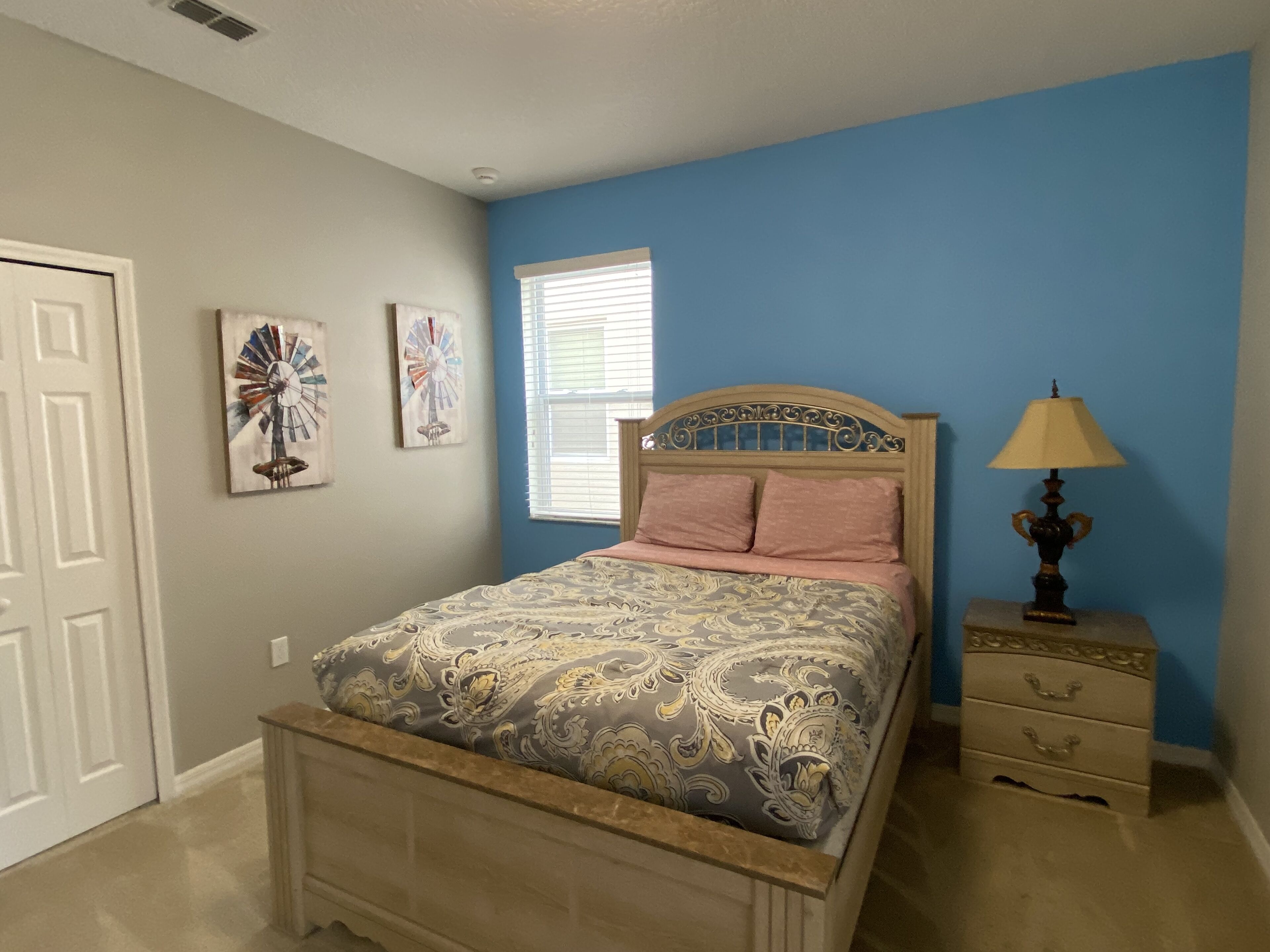 A bedroom with a bed, a nightstand, a lamp, and two wall art pieces.