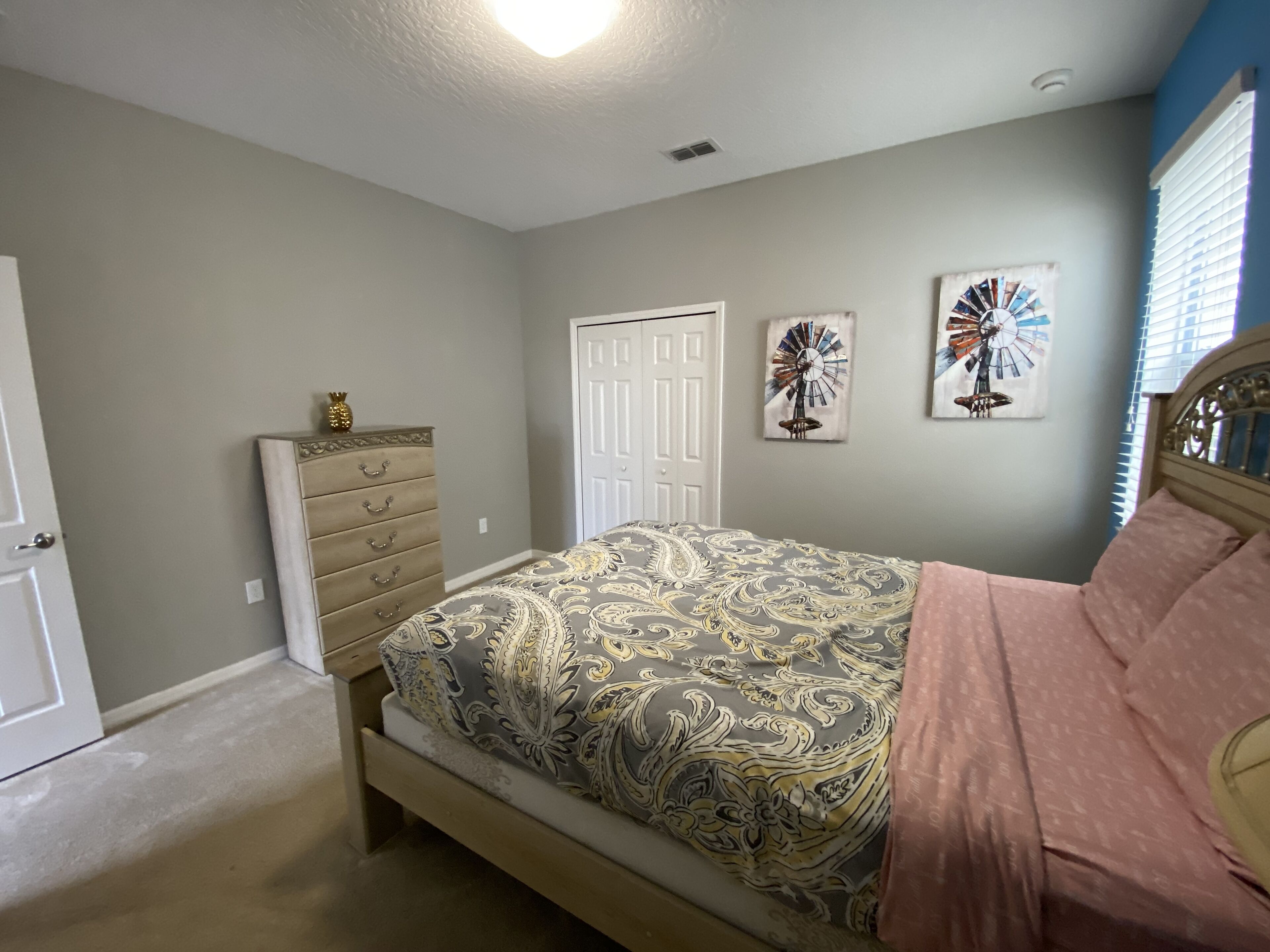 A bedroom with a bed, dresser, and two wall art pieces.