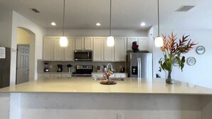 Una cocina moderna con gabinetes blancos, electrodomésticos de acero inoxidable e iluminación colgante.