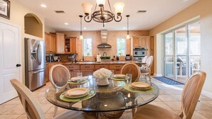A modern kitchen with a glass dining table, wooden chairs, and a chandelier. - Luxury Resort Style, Heated Pool, 10 Mins to Gulf Mexico Beaches (Bradenton)