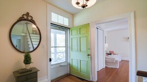 Une pièce avec une porte verte, un plancher en bois, une petite table sur laquelle se trouve une plante, et un miroir accroché au mur.