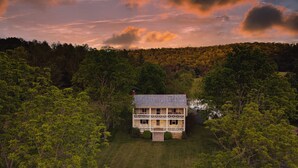 Une maison à deux étages entourée d’une forêt dense.