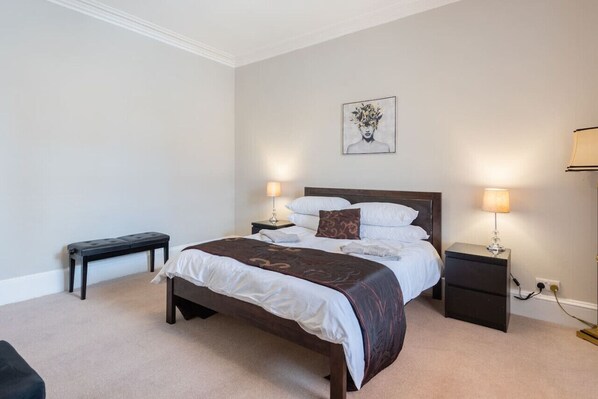 A neatly arranged bedroom with a bed, bedside tables, a bench, and a wall-mounted artwork. - Scotston Villa - 5 bedroom house with large private back garden & hot tub (Forfar)