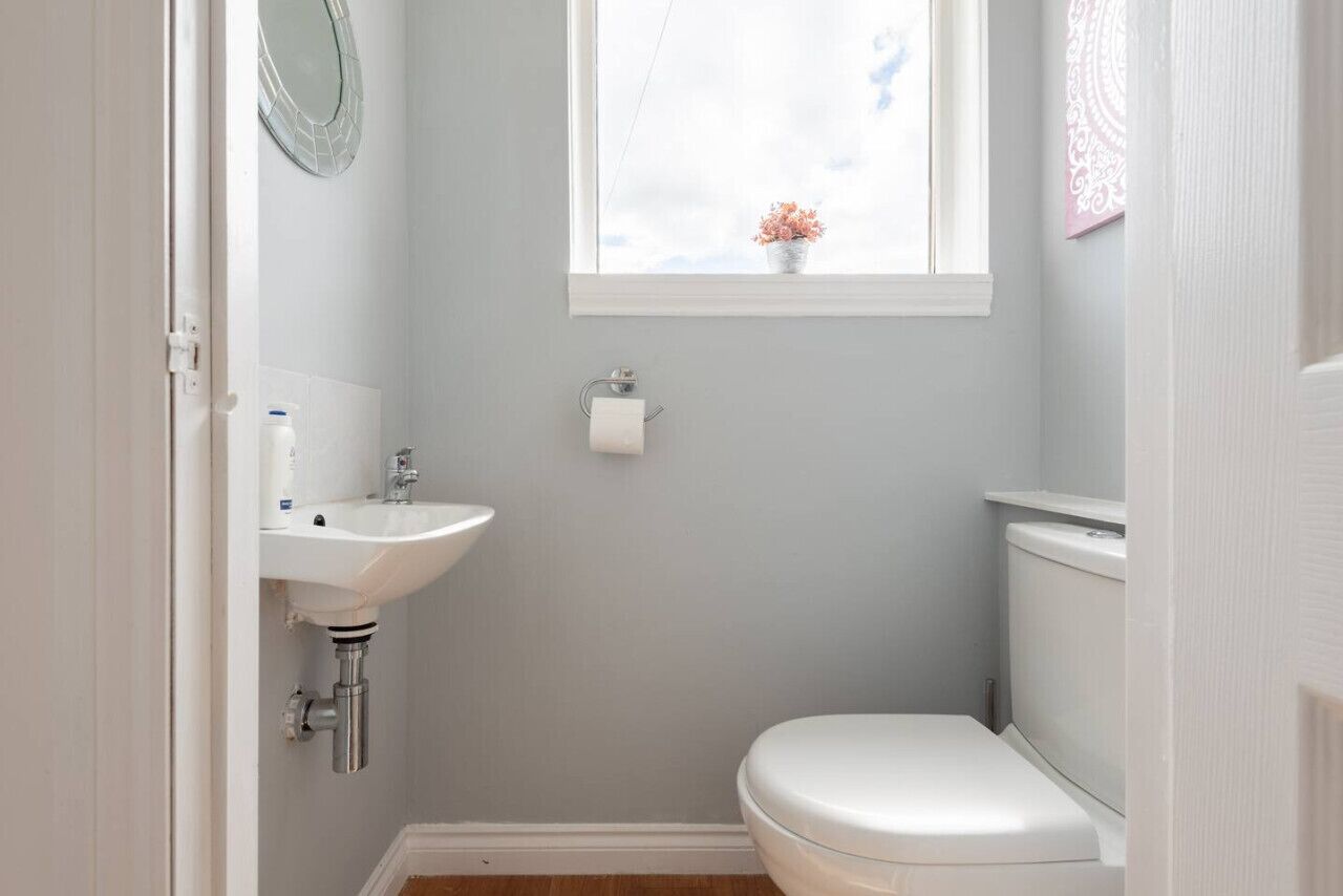 A small bathroom with a white sink, toilet, and a window above the toilet.