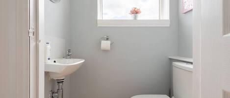 A small bathroom with a white sink, toilet, and a window above the toilet.