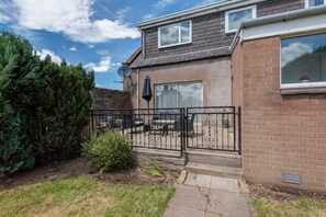 A residential house with a brick exterior, a satellite dish, and a fenced patio area with outdoor furniture. - Scotston Villa - 5 bedroom house with large private back garden & hot tub (Forfar)