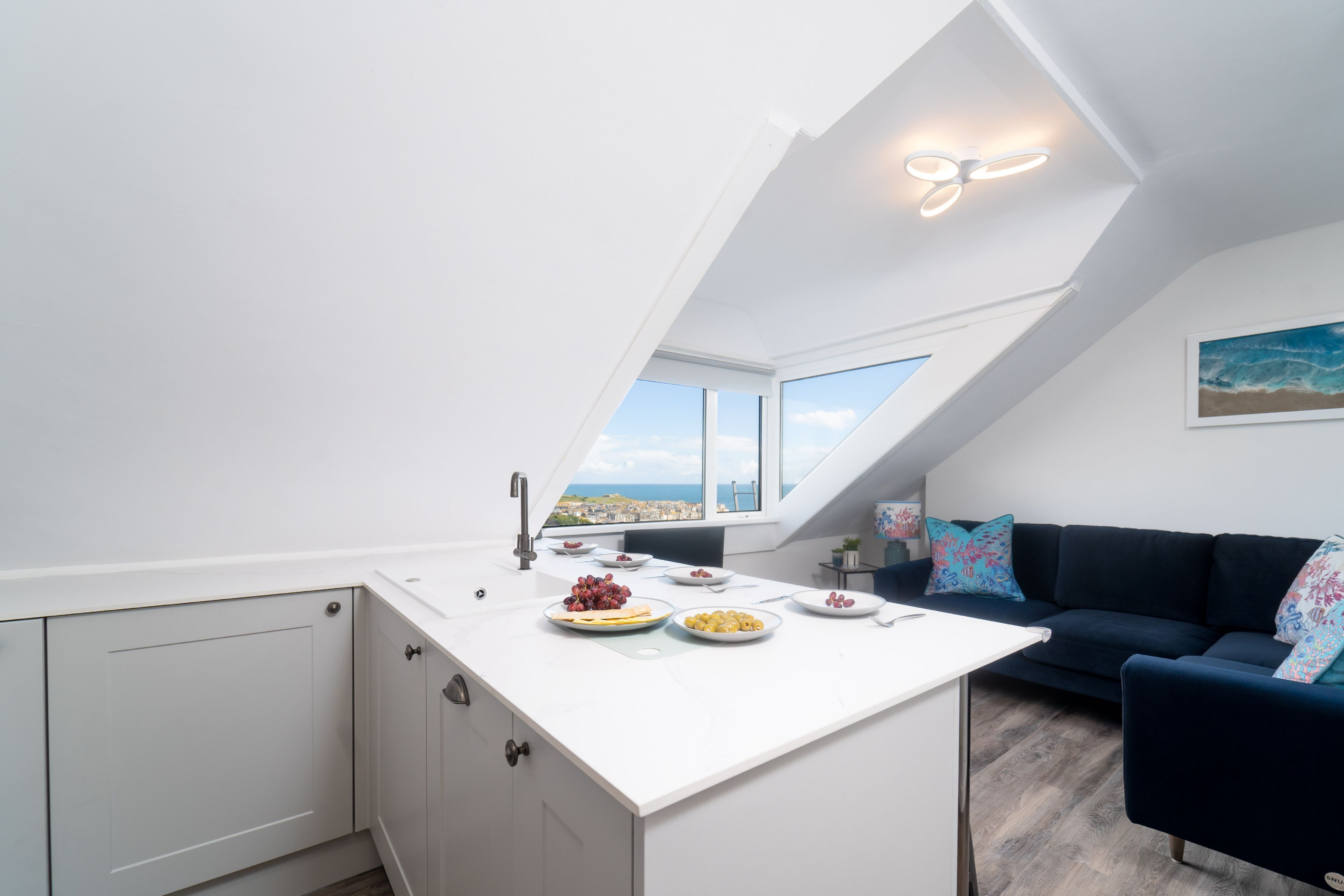 A modern kitchen with a white countertop, a built-in oven, and a view of the city through large windows.