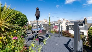En takterrass med ett bord och stolar, omgiven av grönska och en staty.