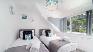 Ett modernt hotellrum med två sängar, en trappa och ett stort fönster med utsikt över grönområden.