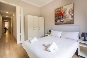 Una camera d'albergo con un letto grande, un armadio, un quadro raffigurante una scena di strada e un corridoio che conduce a un'altra stanza.