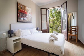 Een hotelkamer met een bed, nachtkastje, stoel en raam met uitzicht op een balkon en bomen.