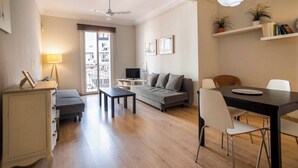 Una sala de estar moderna con un sofá, una mesa de comedor con sillas, un ventilador de techo y vistas al exterior por una puerta corrediza.