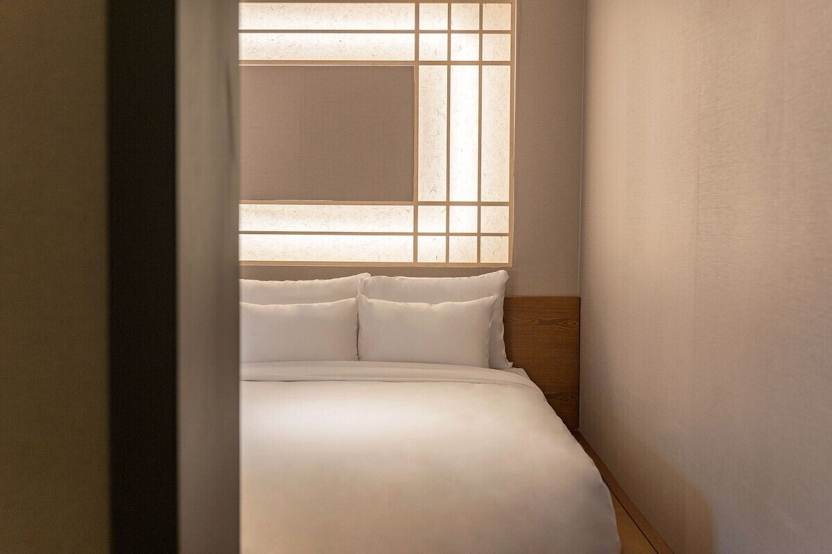 Una habitación pequeña con cama, cabecera de madera y ventana con diseño de celosías.