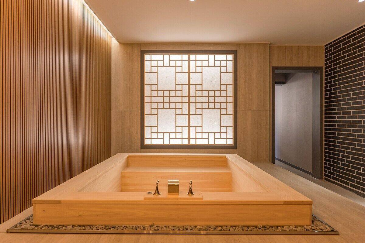 A modern spa room with a wooden floor, a large wooden bathtub, and a decorative wall with a geometric pattern.