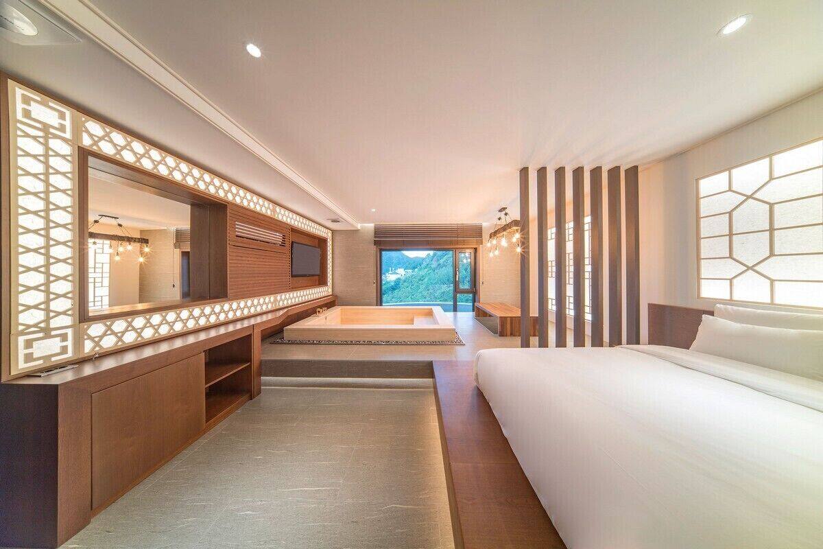 A modern hotel room with a large bed, a TV, a wooden console, and a view of the outdoors.
