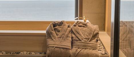 A window with a view of the sea, a wooden bench, and two towels placed on the bench.