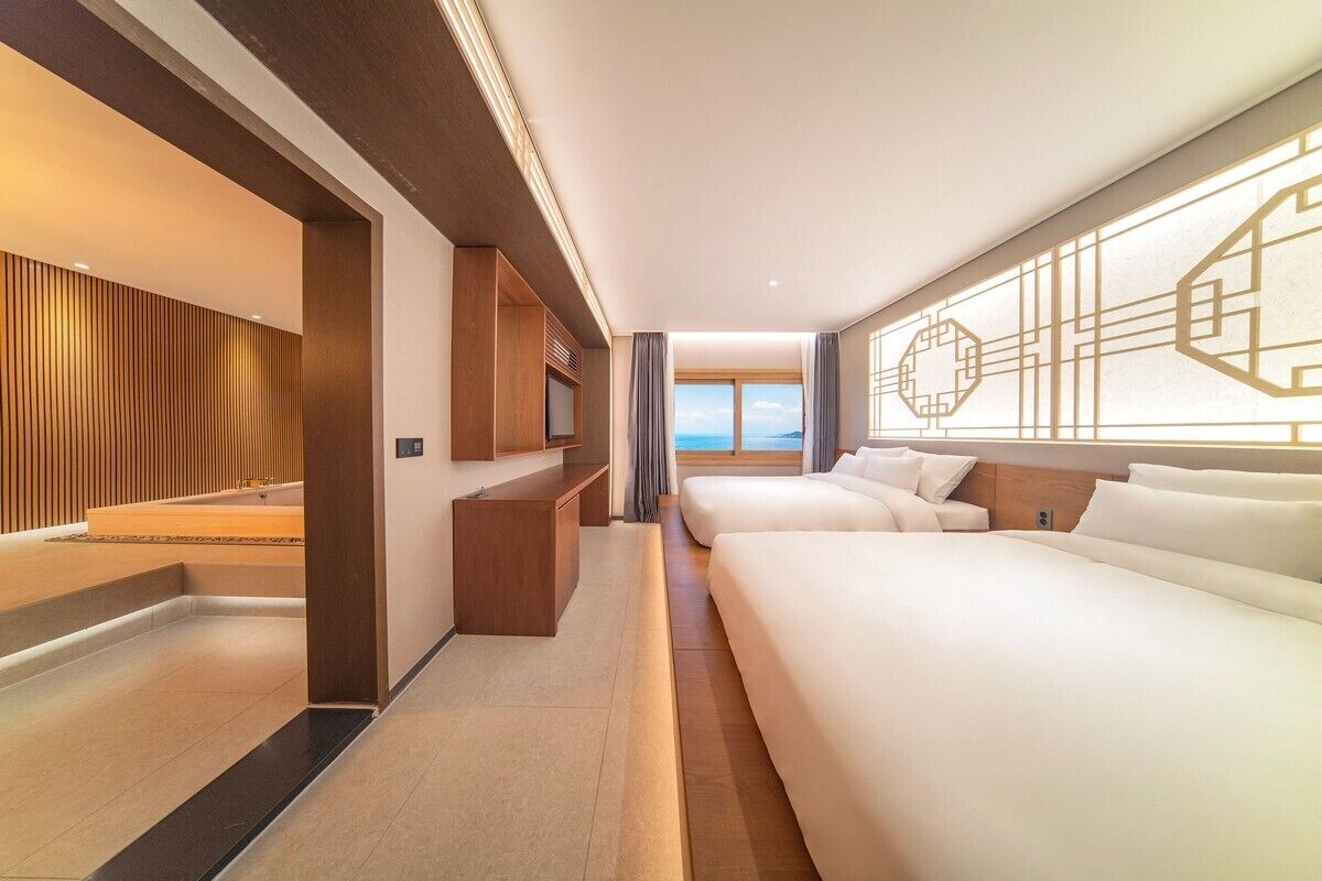 A modern hotel room with a large bed, a desk, and a view of the sea.