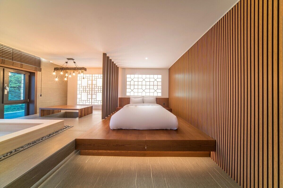 A modern bedroom with a large bed, a wooden floor, a built-in bench, and a large window with a geometric pattern.