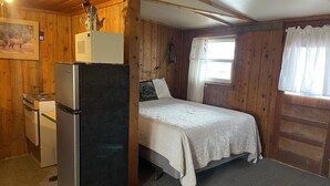 A compact room with a bed, a refrigerator, a stove, and a window with curtains. - Relaxing Cabin in the heart of Red Feather Lakes!! (Red Feather Lakes)