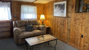 A cozy living room with a leather sofa, a coffee table, a lamp, and a framed picture on the wall. - Relaxing Cabin in the heart of Red Feather Lakes!! (Red Feather Lakes)
