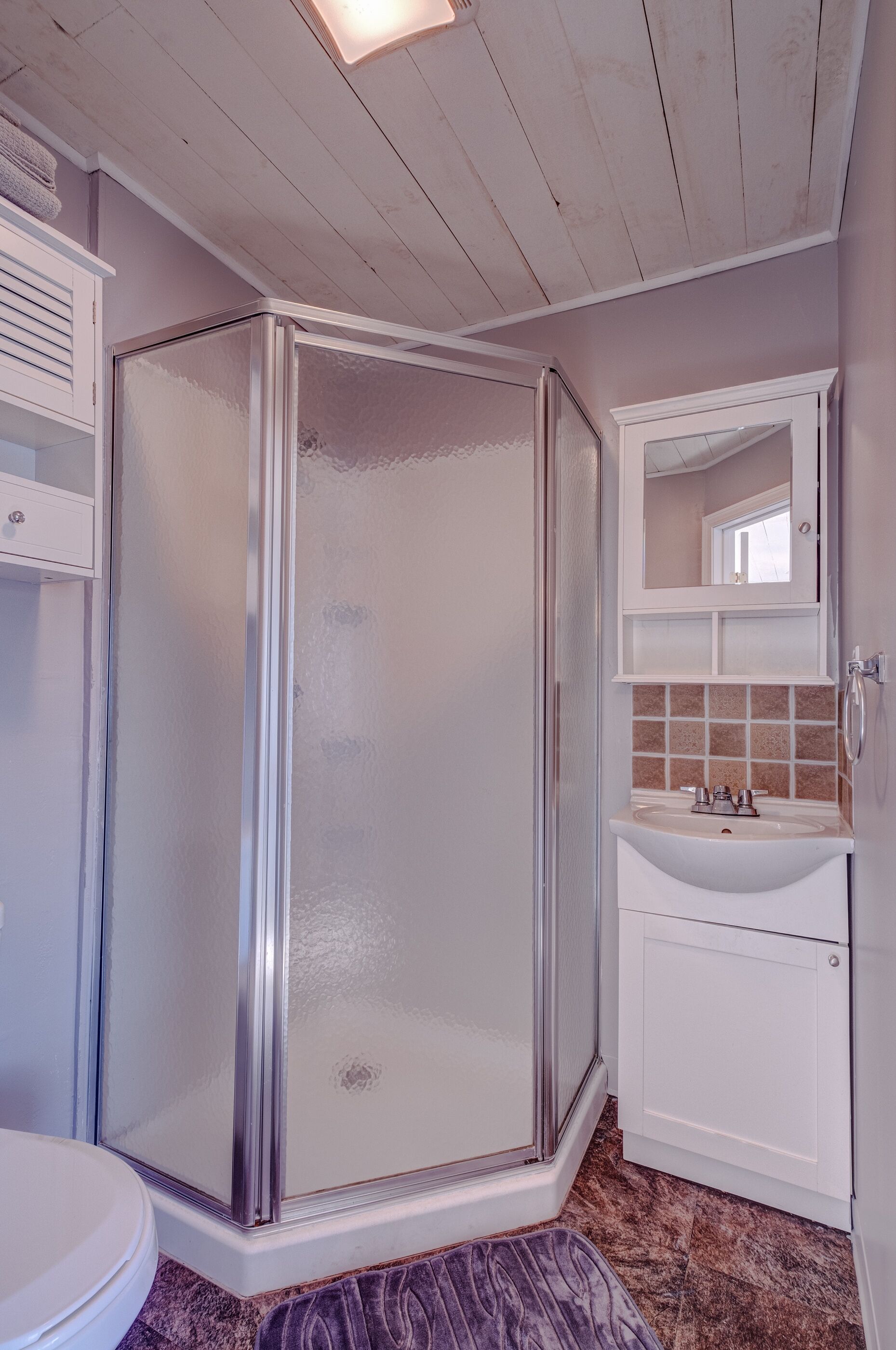 A bathroom with a glass-enclosed shower, a sink, and a mirror above it.