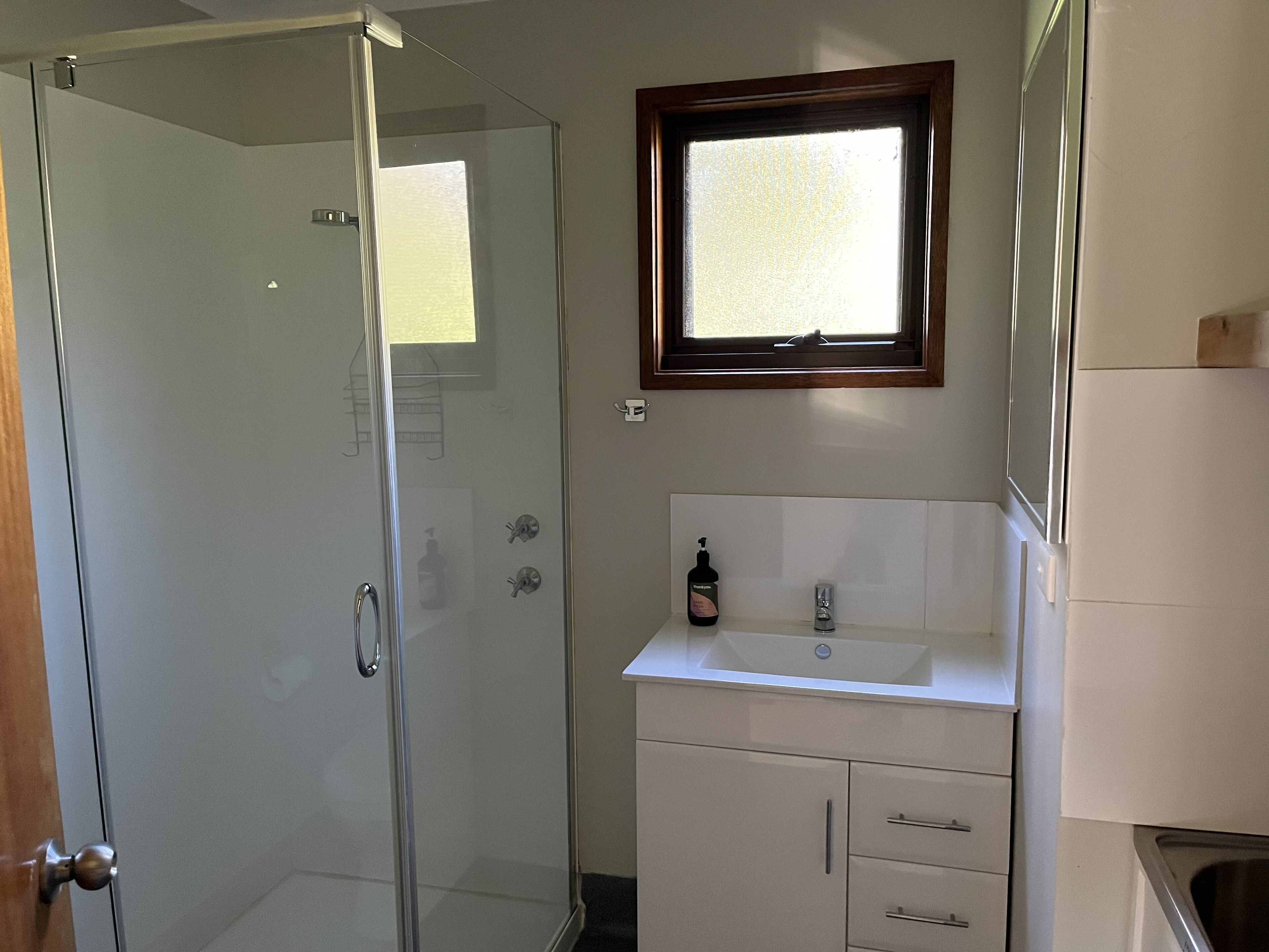 Un baño con cabina de ducha de vidrio, un lavamanos con espejo y una ventana que deja entrar luz natural.