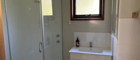 Un baño con cabina de ducha de vidrio, un lavamanos con espejo y una ventana que deja entrar luz natural.