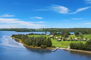 A lakeside property with multiple cabins, a dock, and lush greenery. - Black Bream Point Cabins (North Narooma)
