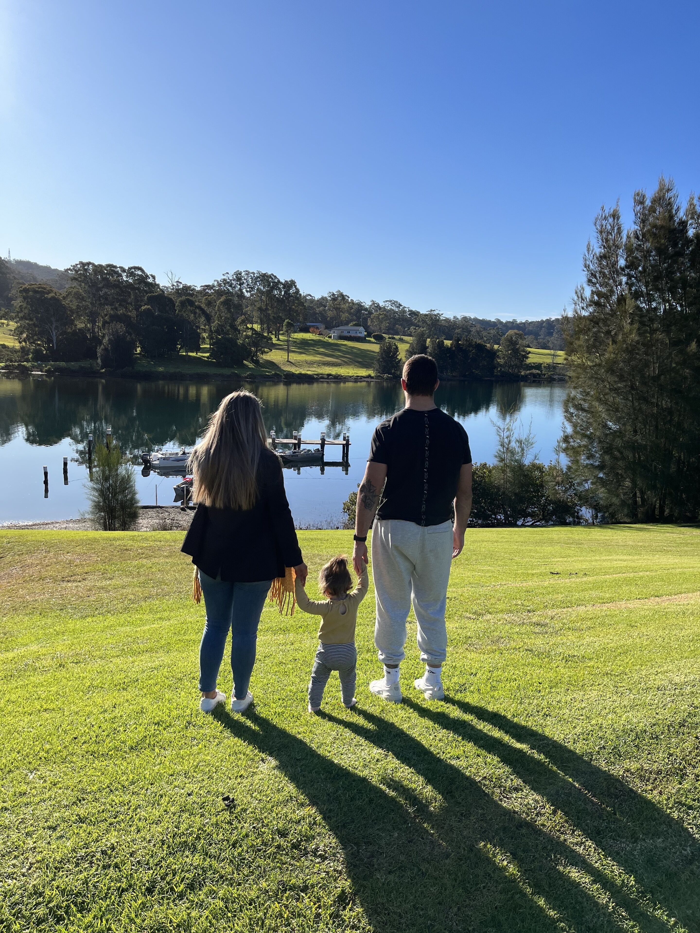 Une famille se promène sur une pelouse, avec un lac et des arbres en arrière-plan.