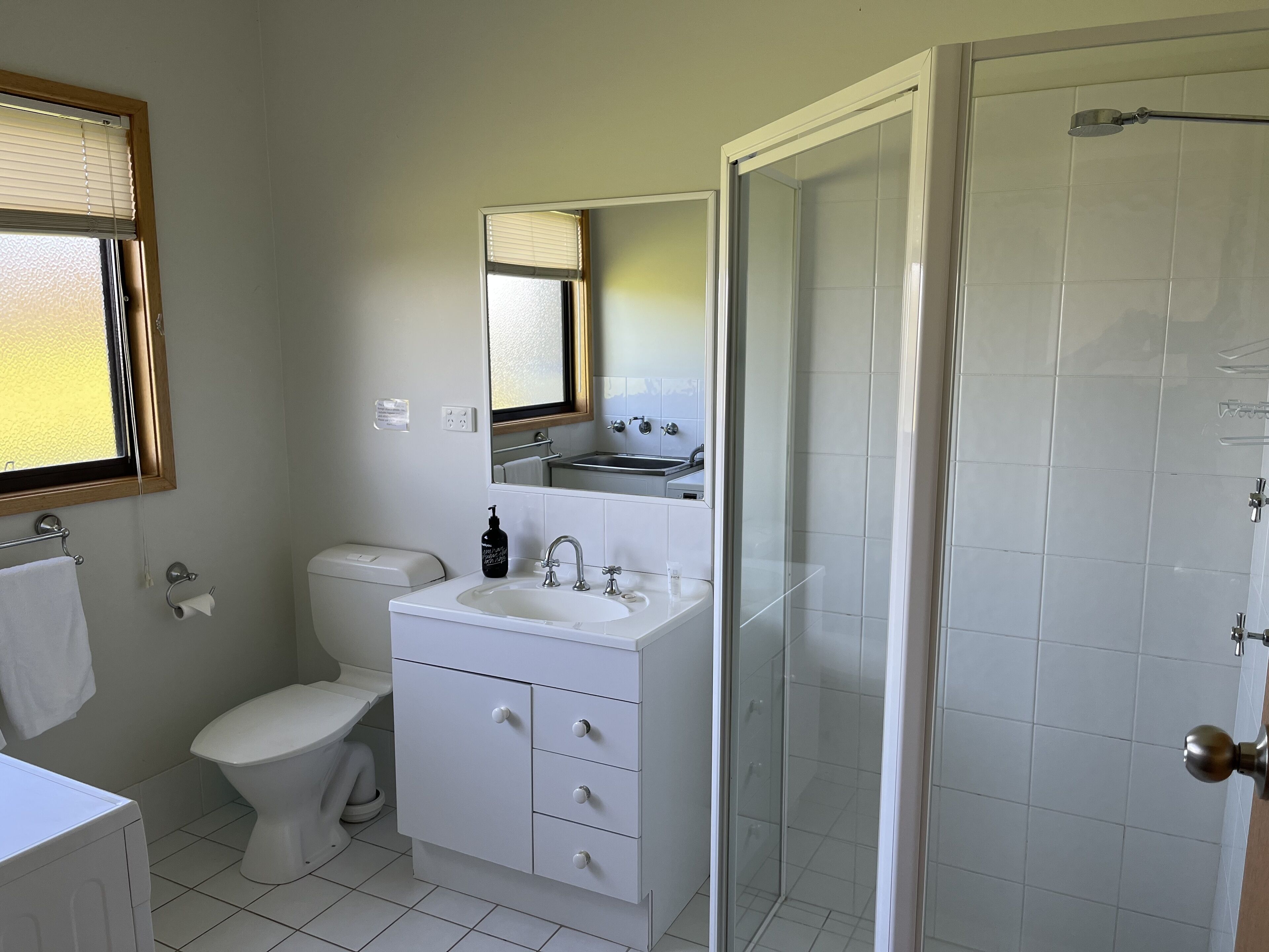 A bathroom with a toilet, sink, mirror, and shower.