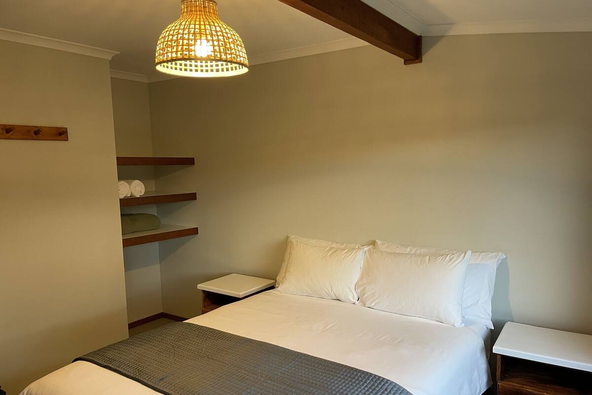 A bedroom with a bed, bedside tables, a hanging light fixture, and built-in shelves.