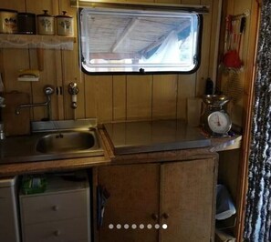 Een compacte keuken met een raam, houten kastjes, een spoelbak en een weegschaal.