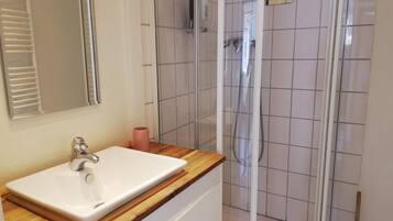 Ein Badezimmer mit weißem Waschbecken, einer Holztischplatte und einer Duschkabine aus Glas.