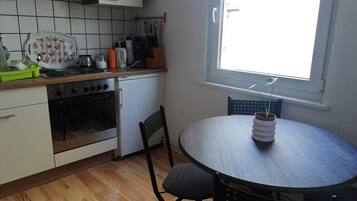 Eine Küche mit Herd, Backofen und Spüle. Ein Esstisch mit Stühlen und ein Fenster mit Ausblick.