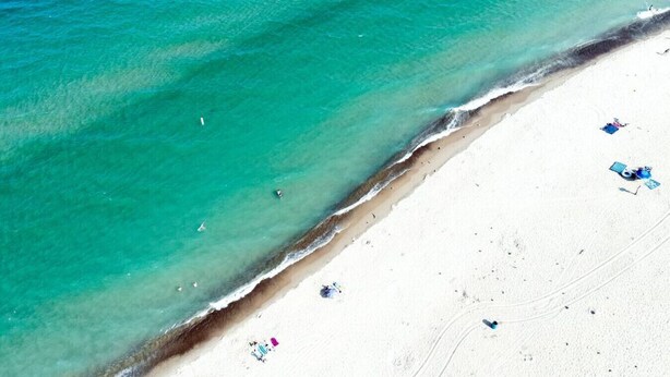 Een strand met helder turquoise water en wit zand. Enkele mensen en strandstoelen zijn zichtbaar.
