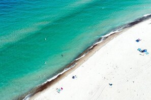 Een strand met helder turquoise water en wit zand. Enkele mensen en strandstoelen zijn zichtbaar.