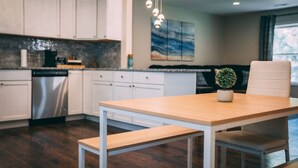 Een moderne keuken met witte kasten, een RVS vaatwasser, een houten eettafel met banken en hanglampen.