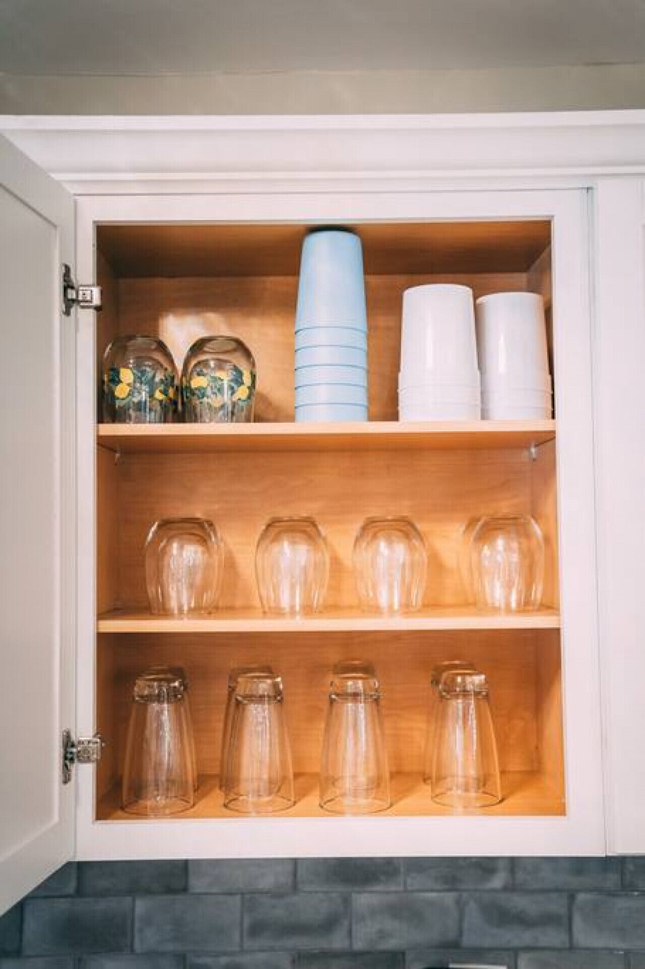 Een kast met verschillende planken, gevuld met diverse glazen potten en plastic bekers.